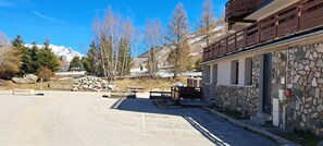 Ein Gebäude aus Stein mit einem Balkon, einer gepflasterten Fläche mit Bänken und einer Bergkulisse im Hintergrund.
