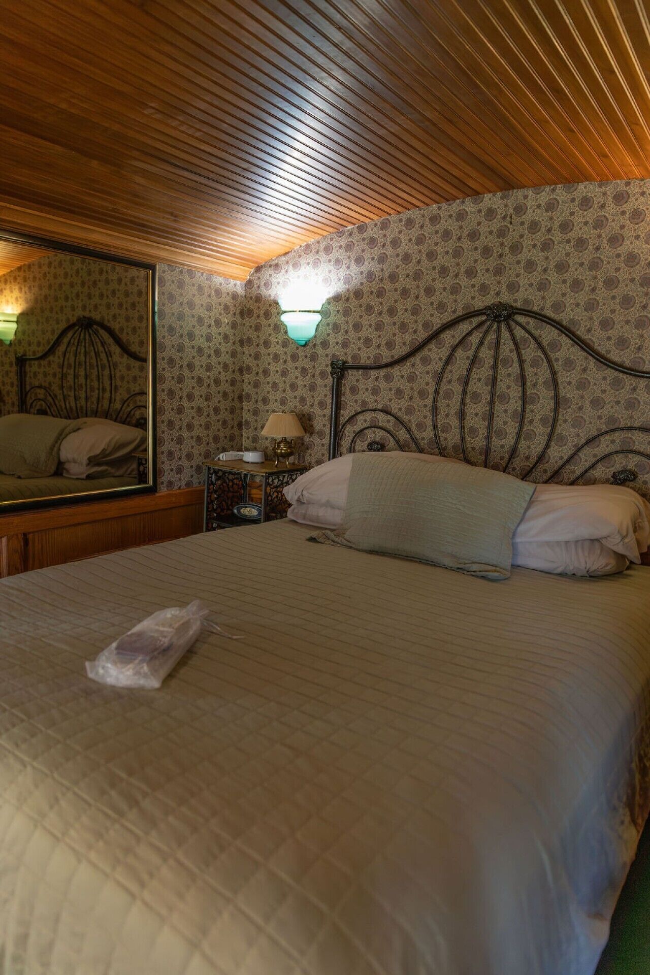 A neatly made bed with a pillow, a bedside table with a lamp, and a mirror on the wall.