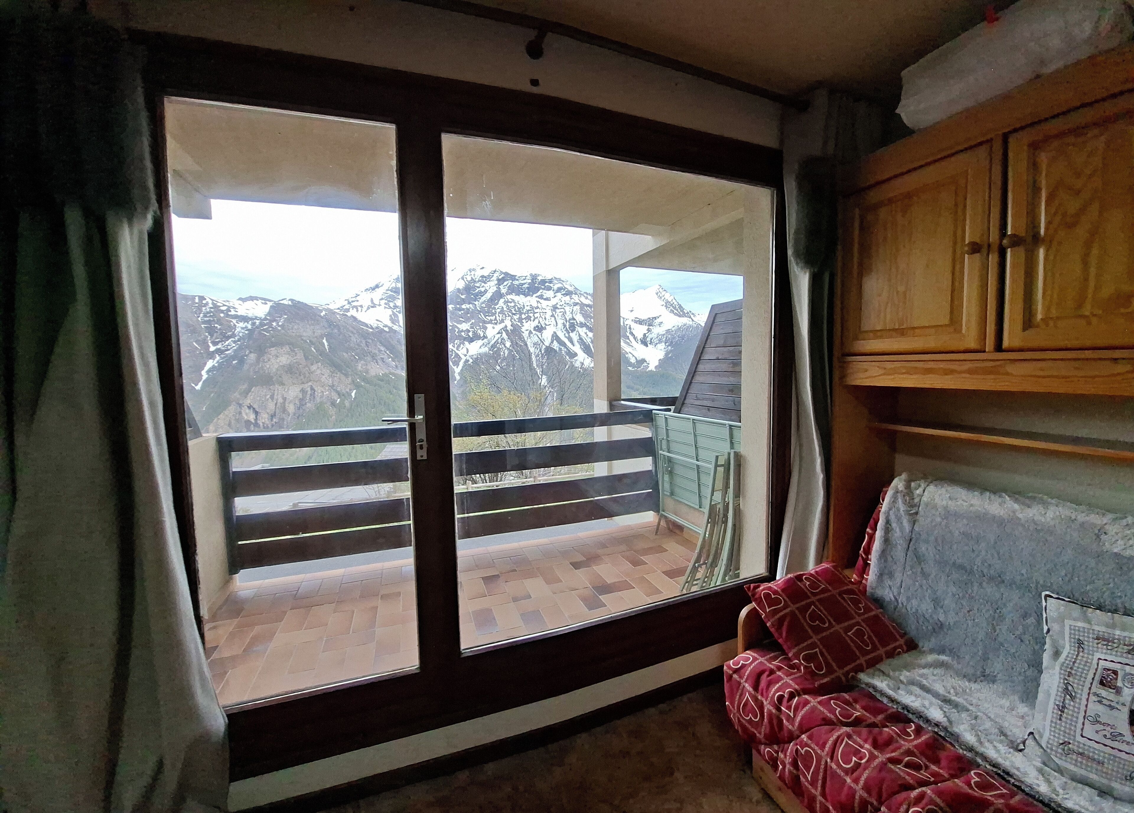 A room with a sliding glass door leading to a balcony, wooden cabinets, and a patterned cushion.