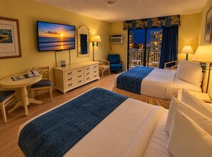 A hotel room with two beds, a desk, a chair, a dresser, and a large window with a view of the city at night. - The Coastal SM | Fifty Oh Four Oh Three (Myrtle Beach)