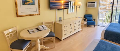 A hotel room with a bed, a desk with chairs, a dresser, a television, and a window with a view.
