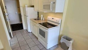 Una cocina compacta con armarios blancos, microondas, estufa y un cubo de basura.