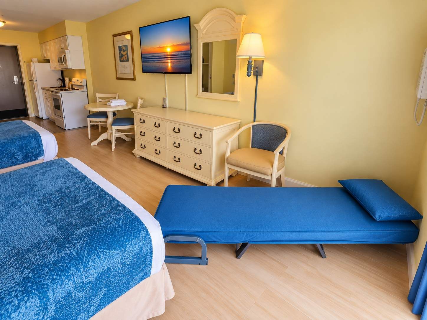 A hotel room with two beds, a desk, a chair, a dresser, and a TV displaying a sunset.