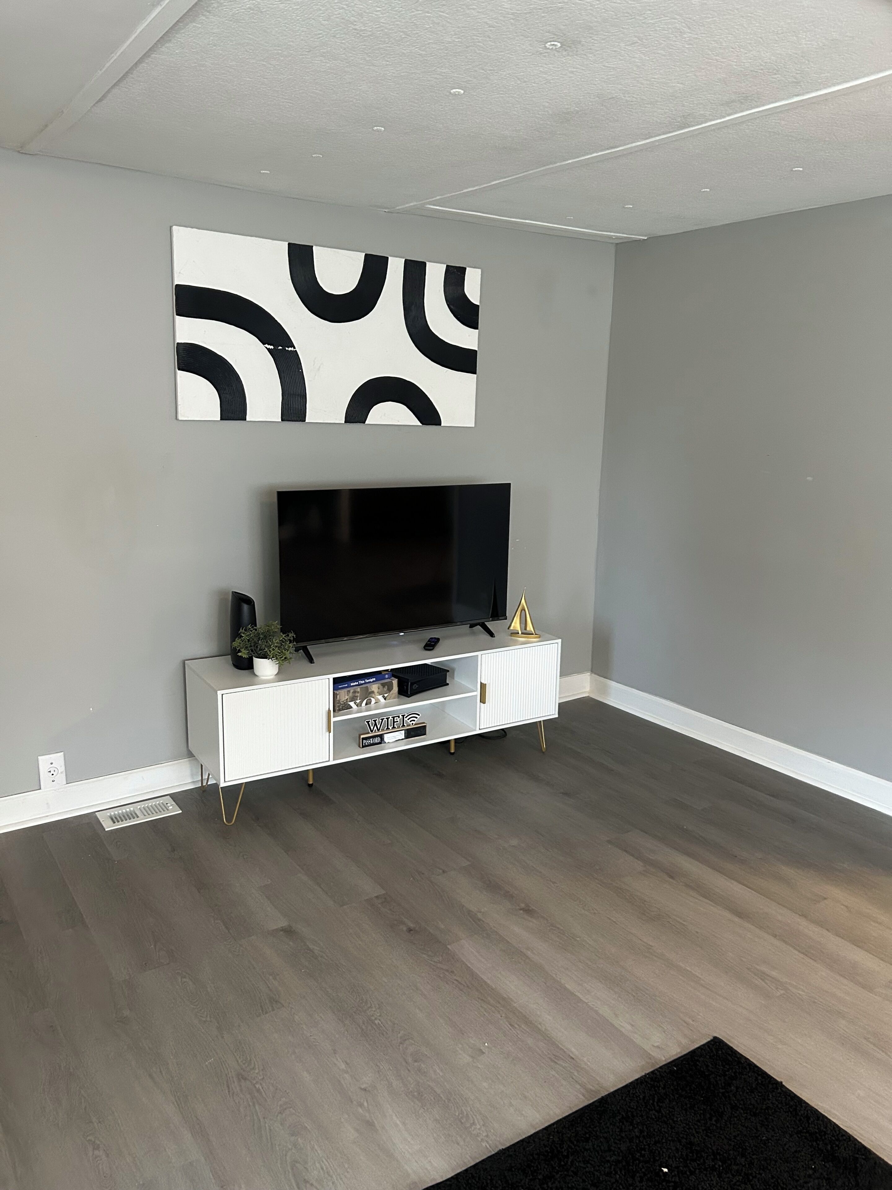 Una sala moderna con televisor de pantalla plana, consola blanca y alfombra negra.