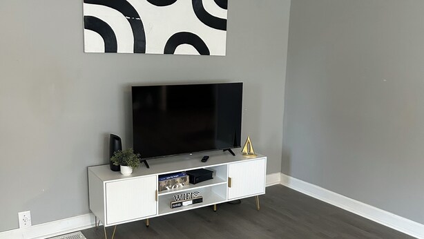 Una sala moderna con televisor de pantalla plana, consola blanca y alfombra negra.