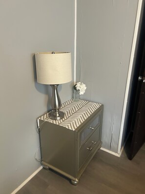 A corner with a lamp on a patterned nightstand, a small vase with flowers, and a door. - 2-bedroom Zen minimalist mobile home by beaches and more! (Jacksonville)