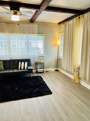 A living room with a black sofa, a black rug, a ceiling fan, and a floor lamp. - 2-bedroom Zen minimalist mobile home by beaches and more! (Jacksonville)