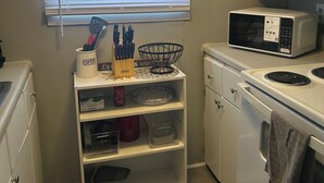 Una cocina compacta con armarios blancos, un microondas, una estufa y una ventana con persianas.