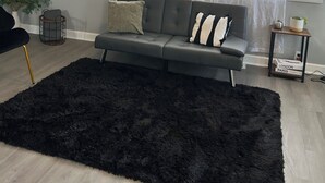 Una sala de estar moderna con un sofá gris oscuro, un tapete mullido negro y un ventilador de techo.