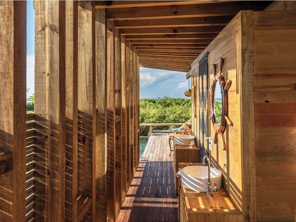 Terraza de madera que lleva a un baño con vistas a la vegetación.