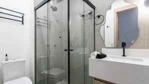 A modern bathroom with a glass-enclosed shower, a toilet, and a vanity with a mirror. - Conforto prox metrô e Estacionamento (São Paulo)