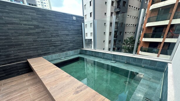 A rooftop swimming pool with a wooden deck and a dark tiled wall. - Conforto prox metrô e Estacionamento (São Paulo)