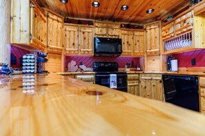 A wooden kitchen with a central island, a microwave, stove, and dishwasher. - Bear-Themed Lodge / Sleeps 10 / Private Beach (Millersburg)