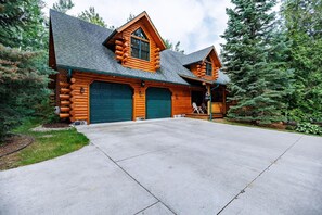 A log cabin with two garage doors, a covered porch, and a driveway. - Bear-Themed Lodge / Sleeps 10 / Private Beach (Millersburg)