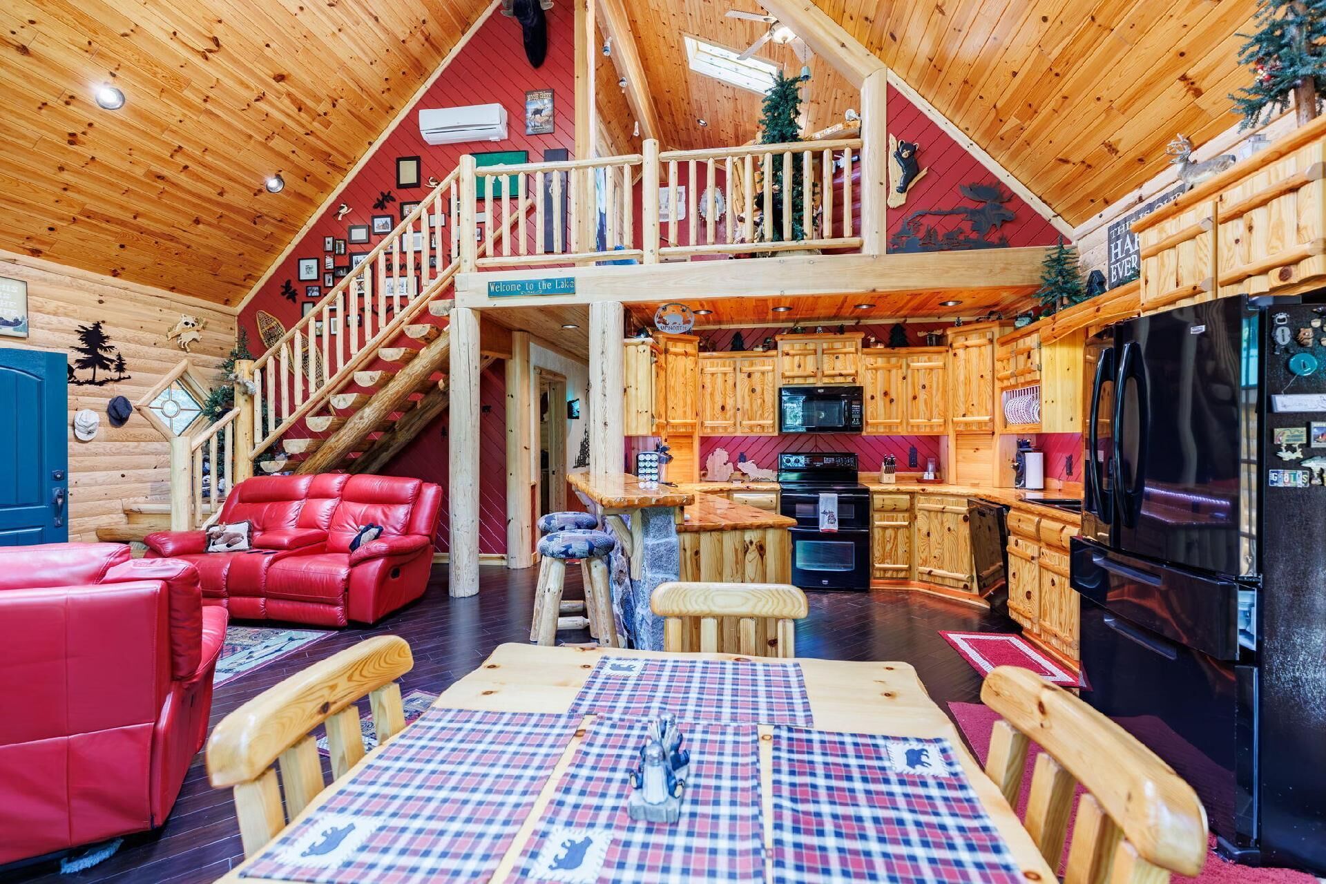 A cabin interior with a dining area, kitchen, and a staircase leading to a loft.