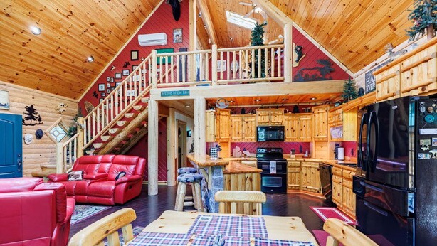 Een chaletinterieur met een eethoek, keuken en een trap naar een slaapverdieping.