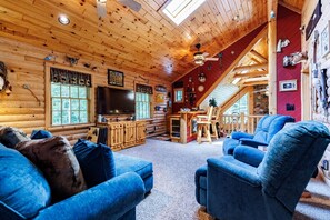 A log cabin interior with a TV, wooden furniture, and a stone wall. - Bear-Themed Lodge / Sleeps 10 / Private Beach (Millersburg)