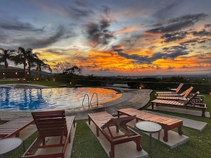 A pool area with lounge chairs and tables, surrounded by a landscaped garden, under a sunset sky. - Modern Lakeview Penthouse: Pool/Gym/Restaurant (Río Oro)