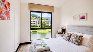 Een hotelkamer met een groot bed, uitzicht op een gebouw en water, en een raam met een zonnescherm.