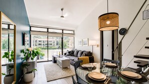Een moderne woonkamer met een glazen eettafel, bank en grote ramen.