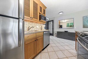 A modern kitchen with stainless steel appliances, wooden cabinets, a tiled backsplash, and a large mirror above the sink. - Mahina Surf 123 & 124 (Lahaina)