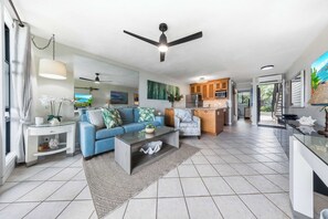 A modern living room with a blue sofa, a coffee table, and a ceiling fan. - Mahina Surf 123 & 124 (Lahaina)