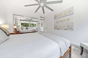 Une chambre avec un grand lit, un ventilateur de plafond, une vue sur une autre pièce et des œuvres d’art murales.
