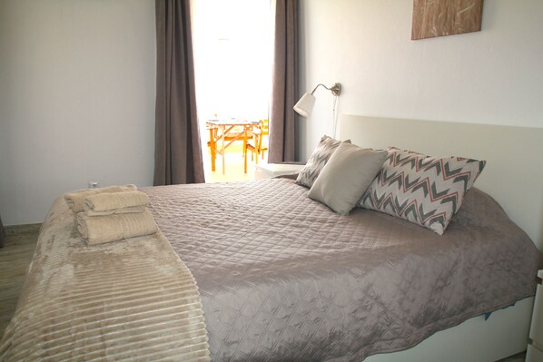 A neatly made bed with a quilted cover and pillows, a bedside lamp, and a window with curtains.
