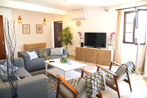 Ein Wohnzimmer mit Sofa, Sesseln, Couchtisch, Fernseher und einer Pflanze.
