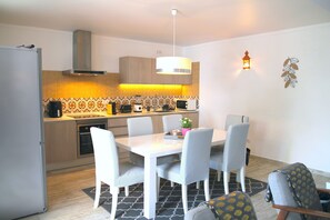 A modern kitchen with a dining area, featuring a white table, grey chairs, and a patterned backsplash.