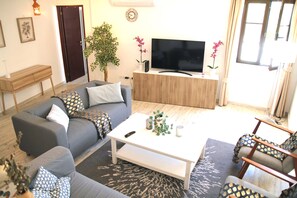 A living room with a grey sofa, a white coffee table, a TV on a wooden stand, and a potted plant.