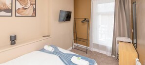 Habitació d'hotel amb un llit, una televisió penjada a la paret, un estenedor i una finestra amb cortines.