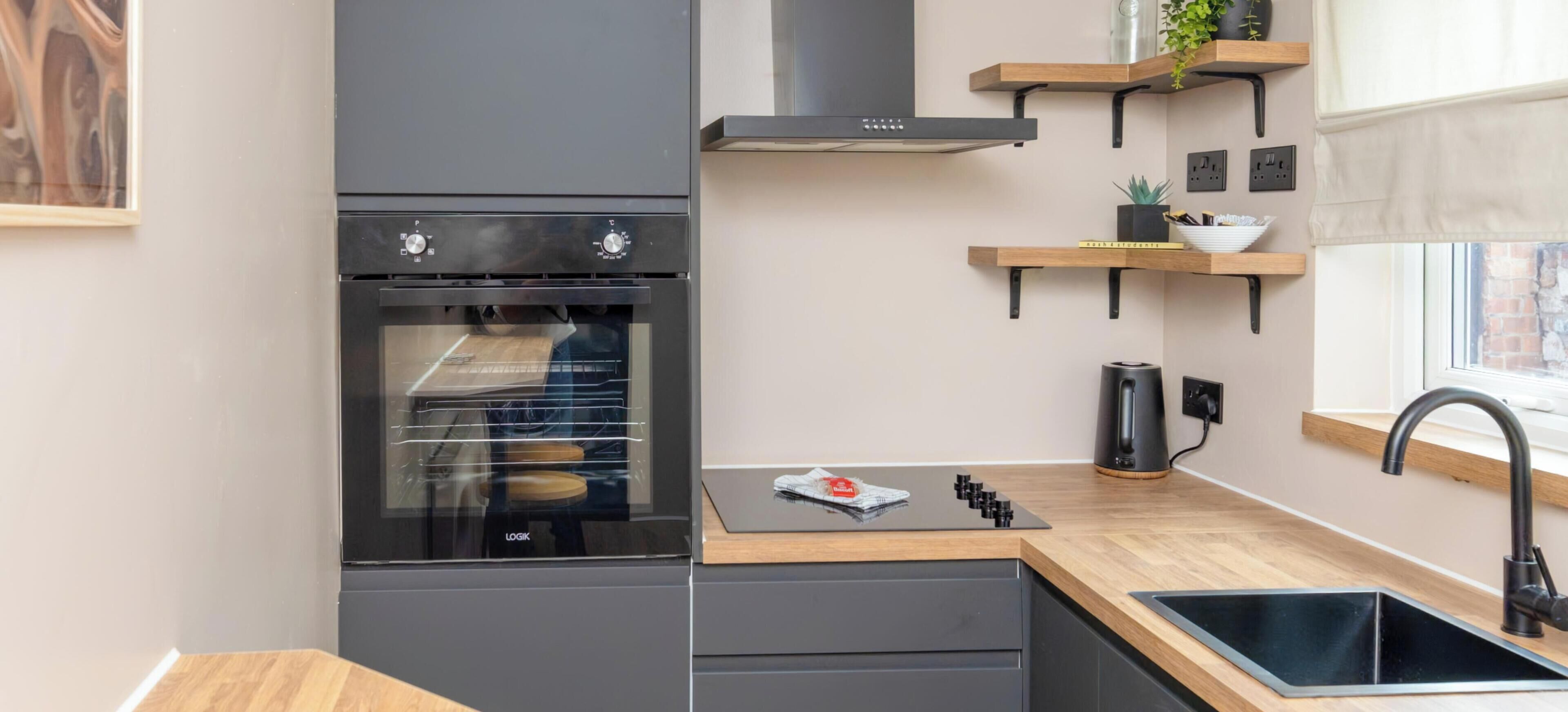 A modern kitchen with a built-in oven, wooden countertop, and a black faucet.