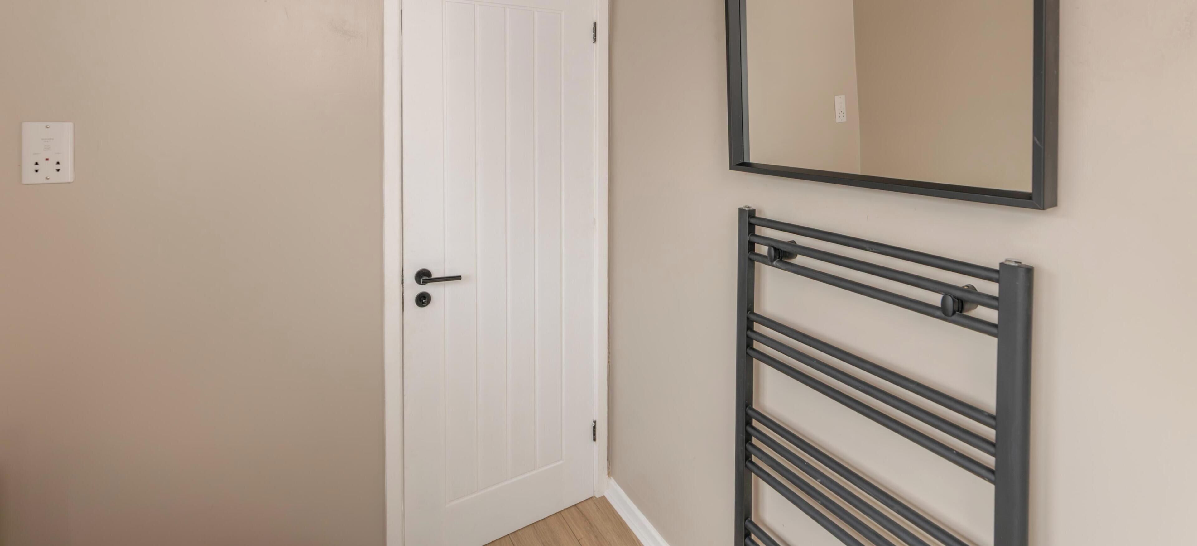 A white door with a handle, a wall-mounted mirror, and a metal radiator.