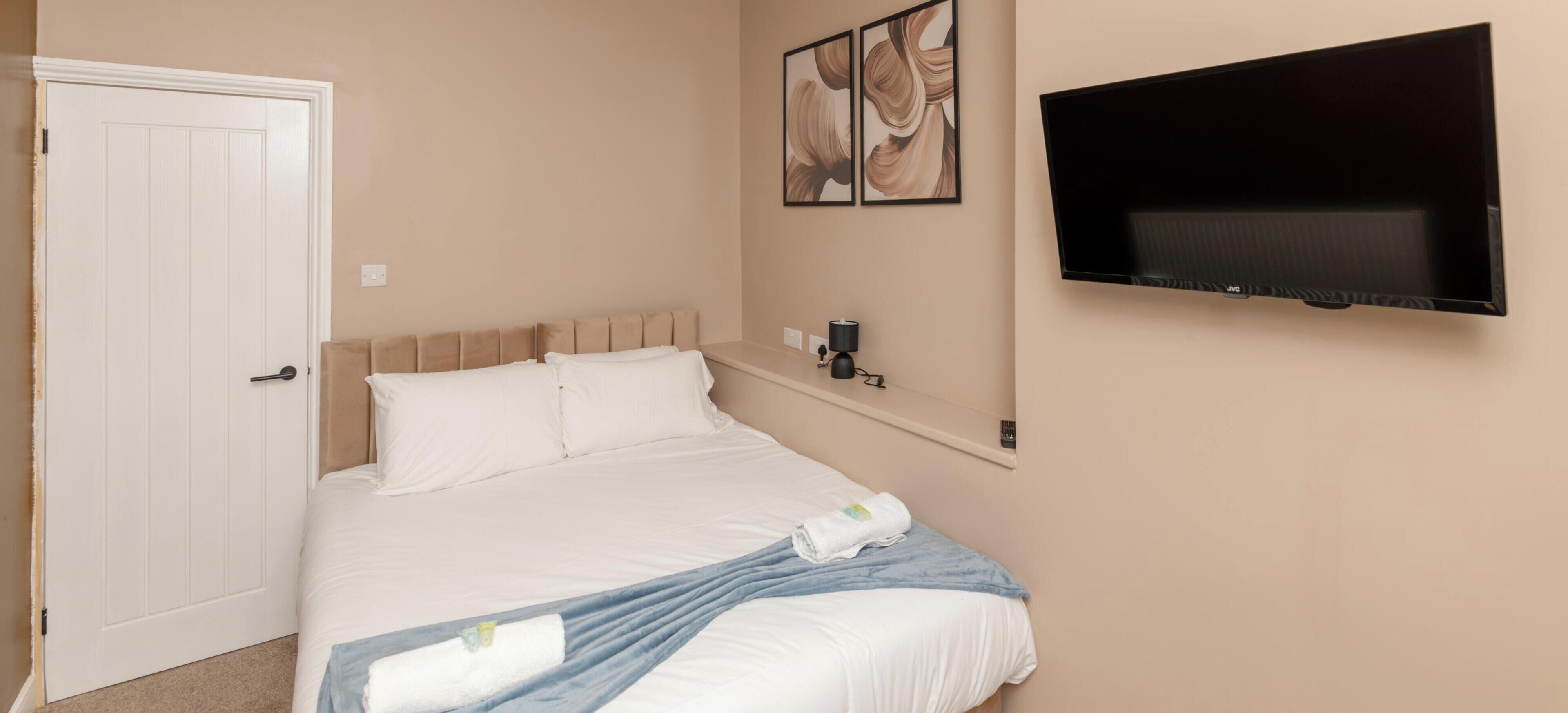A hotel room with a bed, a TV mounted on the wall, and a door.