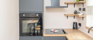 A modern kitchen with a built-in oven, wooden shelves, and a kettle on the countertop.