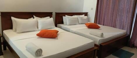 A hotel room with two single beds, each with white bedding and pillows, and a wooden headboard.