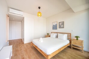 A bedroom with a wooden bed, white bedding, a bedside lamp, a wall-mounted air conditioner, and two framed artworks. - GuestReady-Modern Retreat with Balcony Views (Lisbon)
