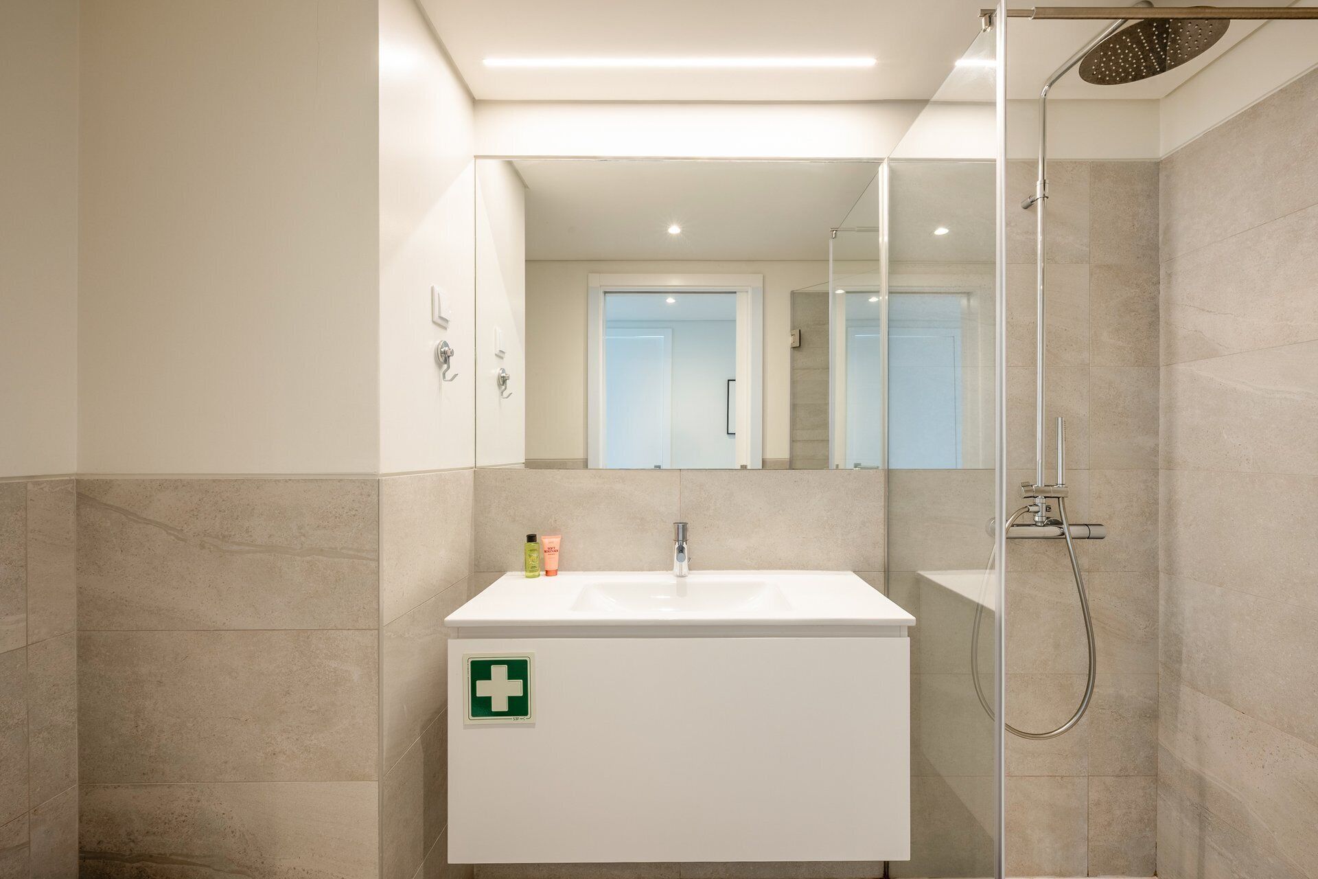 Une salle de bain moderne avec un lavabo blanc, une douche en verre et un miroir au-dessus du lavabo.