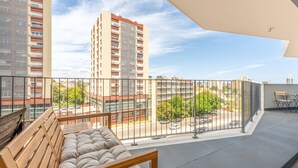 Ein Balkon mit einer hölzernen Sitzbank, einem Metallgeländer und Blick auf einen Parkplatz sowie Gebäude.