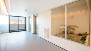 Ein modernes Interieur mit einer Glastür, die auf einen Balkon führt, einem weißen Fliesenboden und Blick auf Gebäude im Freien.