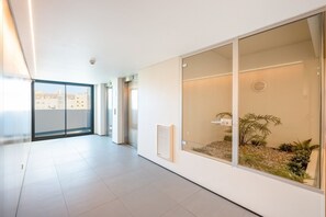 A modern interior with a glass door leading to a balcony, a white tiled floor, and a view of buildings outside. - GuestReady-Modern Retreat with Balcony Views (Lisbon)