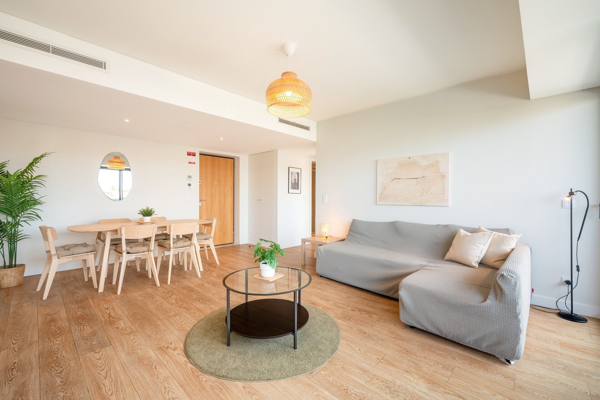Un salon moderne avec une table basse ronde, un canapé gris, un parquet en bois et une grande fenêtre.