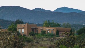 Un bâtiment de style désertique, doté de nombreuses pièces et d’un toit plat, entouré de cactus et d’arbustes.