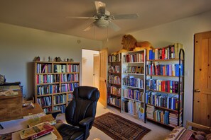 Une pièce dotée d’un ventilateur de plafond, d’une grande bibliothèque remplie de livres, d’un fauteuil en cuir et d’une porte en bois.