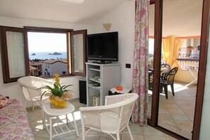 A balcony with a TV, wicker furniture, a small table with a plant, and a view of the sea. - Stunning apartment with a view of the sea, a 700-meter walk from the beach (Santa Maria Navarrese)