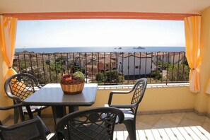 A balcony with a table and chairs, a basket of fruit, and a view of the sea and buildings. - Stunning apartment with a view of the sea, a 700-meter walk from the beach (Santa Maria Navarrese)