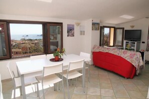 A room with a dining table, chairs, a red sofa, a TV, and a view of the sea. - Stunning apartment with a view of the sea, a 700-meter walk from the beach (Santa Maria Navarrese)