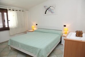 Ein Schlafzimmer mit einem Bett, zwei Nachttischen, einer Lampe auf jedem Tisch, einem Wandbild und einem Fenster mit Vorhängen.