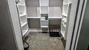 A compact walk-in closet with open shelving, a small shoe rack, and a green box on the middle shelf. - The Rock House | Walk to OSU (Stillwater)